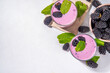 Two glasses of blackberry smoothie, yogurt or milkshake with fresh berry, mint leaves on white table background copy space