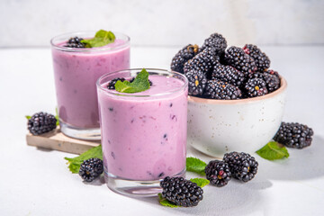 Wall Mural - Two glasses of blackberry smoothie, yogurt or milkshake with fresh berry, mint leaves on white table background copy space