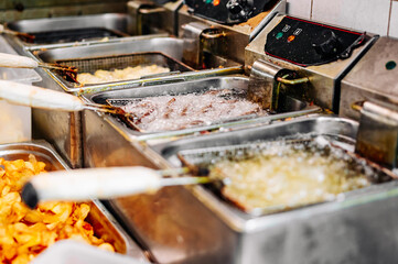 French fries and potato chips deep frying in oil in a commercial metal fryer in a restaurant kitchen