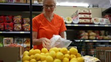 Slow Motion View Of Smiling Happy Pretty Mature Woman Selecting Lemons In A Grocery Store.
