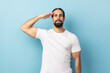 Portrait of serious responsible man bodybuilder with beard giving salute listening to order with serious attentive expression, following discipline. Indoor studio shot isolated on blue background.