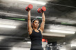 © Dusan Petkovic - A muscular sportswoman in shape is lifting dumbbells over her head in a gym.