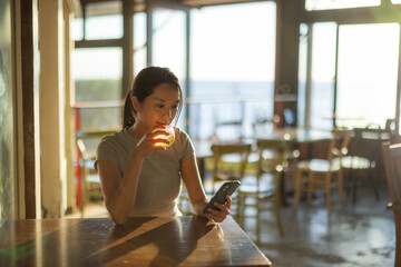 Poster - Woman enjoy her drink and look at the cellphone in cafe at sunset time