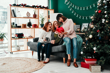 Thank you both very much. Shot of three attractive middle aged women opening presents together while being seated on a sofa during Christmas time.