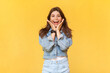 © khosrork - Portrait of excited extremely happy woman in denim jacket standing with palms near face, screaming happily, rejoicing her victory, screaming hurray. Indoor studio shot isolated on yellow background.