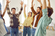 © Studio Romantic - Portrait of a group of excited happy young friends students or colleagues having fun hanging together at home. Men and women standing in a circle raising their hands up enjoying meeting.