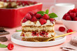 A piece of tiramisu with raspberries on a white plate on the table. Traditional Italian dessert. Selective focus