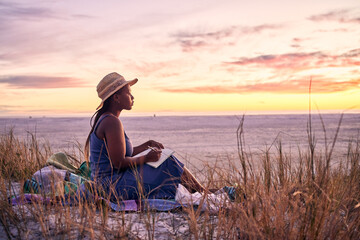 Wall Mural - Black woman, relax and book on beach in sunset with diary or journal for vacation in nature outdoors. African female person relaxing on ocean coast with notebook in morning sunrise and holiday travel