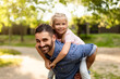 © Prostock-studio - Riding high on love. Happy middle aged father carrying daughter on his back, walking in the park and smiling at camera