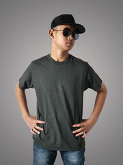 Poster - Young Asian teenage boy wearing black shirt, hat and sunglasses standing with hands on hip over grey background, t-shirt template