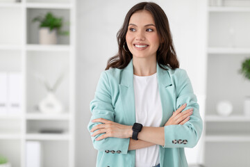 Wall Mural - Cheerful millennial caucasian woman manager boss in suit with crossed arms looks at copy space