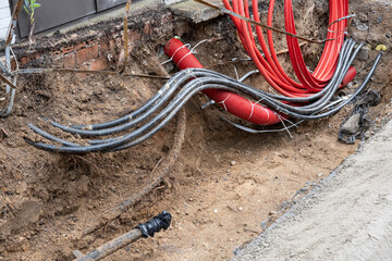 Wall Mural - Electric cables in red corrugated pipe are buried underground on the street. electric cable infrastructure installation. Construction site with A lot of supply energy