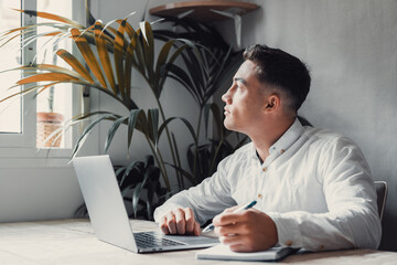 Wall Mural - Thoughtful businessman touching chin, pondering ideas or strategy, sitting at wooden work desk with laptop, freelancer working on online project, student preparing for exam at home.