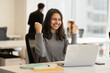 © Maria Vitkovska - Overjoyed Indian woman using laptop computer celebration success sitting in modern office. Happy emotional asian freelancer receive payment, winning money. Successful business concept
