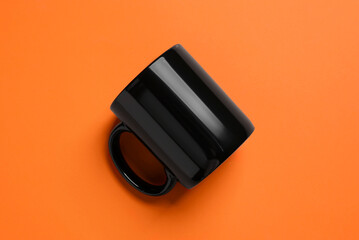 One black ceramic mug on orange background, top view