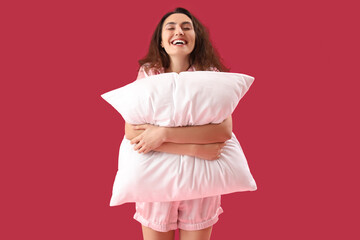 Poster - Young brunette woman in pajamas with pillow on pink background