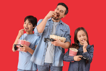 Wall Mural - Little children with their father and game pads eating popcorn on red background