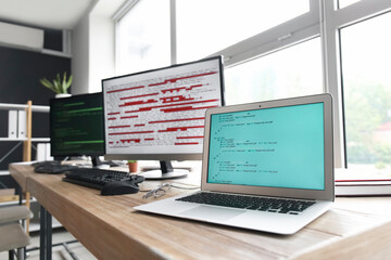 computer monitor and laptop with programming code at programmer's workplace in office, closeup