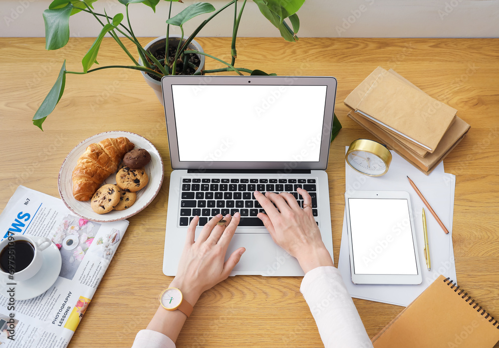 Woman working at table with laptop, cup of coffee, snacks and tablet computer