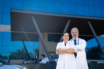 Wall Mural - Indian Senior doctor standing with female doctor in front of hospital