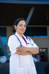 Wall Mural - Medical concept, confident indian female doctor standing out of hospital.