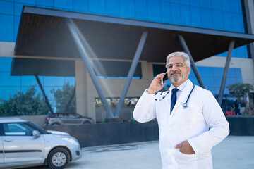 Wall Mural - medical concept. Indian doctor standing out of hospital and talking on mobilephone.