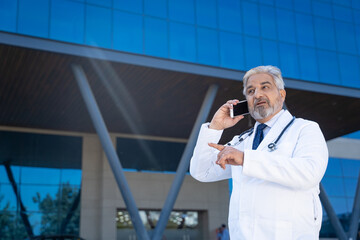 Wall Mural - medical concept. Indian doctor standing out of hospital and talking on mobilephone.