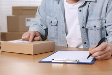 Canvas Print - Seller with parcel and clipboard working at workplace, closeup. Online store