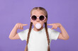 © New Africa - Girl in sunglasses blowing bubble gum on purple background