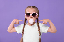Girl In Sunglasses Blowing Bubble Gum On Purple Background