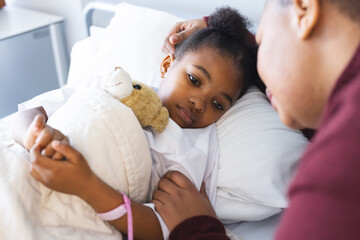 African american girl patient lying on bed with her mother in patient room at hospital