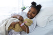 Portrait of happy african american girl patient lying on bed in patient room at hospital