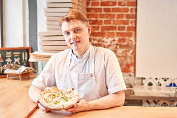 Wall Mural - The chef holds a pizza in his hands. Neapolitan pizza from a wood-fired oven. Pizza is on the plate. Pizza with pear and gorgonzola. Fast delivery of food. 