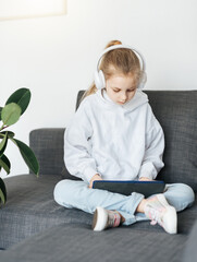 Wall Mural - Little girl with headphones and tablet  at home