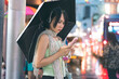 Asian woman wear nostalgia stylish using headphone and flip phone with umbrella on rainy season at night city