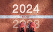 © Dee karen - New year 2024 concept, beginning of success. Text 2024 written on asphalt road and male runner preparing for the new year. Concept of challenge or career path and change.