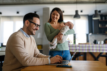 Portrait of business man using laptop working while family in background at home.