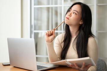 Wall Mural - A thoughtful Asian female college student focuses on planning her project and doing homework