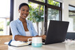 © Wavebreak Media - Portrait of happy african american woman sitting at table using laptop in kitchen