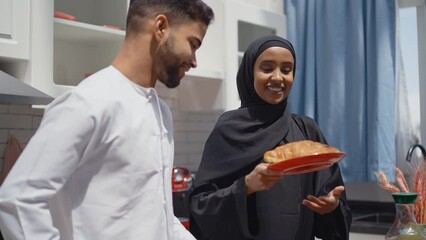 Wall Mural - Happy couple wearing traditional outfits from the emirates spending  time in the kitchen of their beautiful modern apartment in Dubai