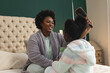 © Wavebreak Media - Happy african american mother and daughter sitting on bed brushing hair at home