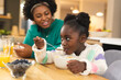 © Wavebreak Media - Happy african american mother and daughter sitting at table eating breakfast at home