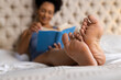 © Wavebreak Media - Feet of biracial woman lying on bed and reading book in bedroom