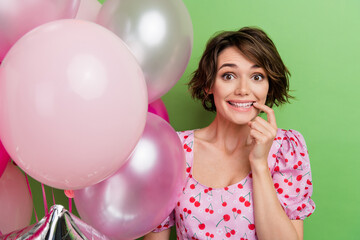 Sticker - Portrait of impressed funky girl with short haircut wear stylish blouse holding bubbles biting finger isolated on green color background