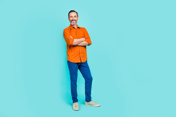 Wall Mural - Full length photo of charming cute guy wear orange shirt arms folded empty space isolated teal color background