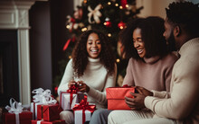 Black African American Dark-skinned Friends Or Family Sitting Near Christmas Tree, Smiling, And Opening Christmas Presents. Holidays And Celebration Concept