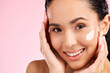 Cream, beauty and face of a woman with skin care, dermatology and natural glow. Closeup of a young female model with a smile for moisturizer, cosmetic space or sunscreen on pink background in studio