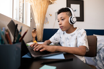 Young boy writes on the computer keyboard at the table in the room