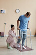 © AnnaStills - Vertical image of patient trying to walk with walker and doctor helping him during his rehabilitation