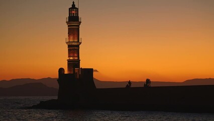 Wall Mural - Silhouettes of people watching a summer sunset on a seawall next to a lighthouse (Chania, Crete)